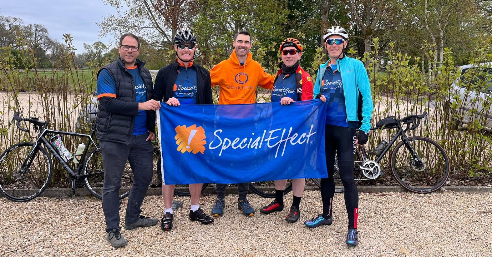 Five men holding a specialeffect flag, four are wearing cycling gear