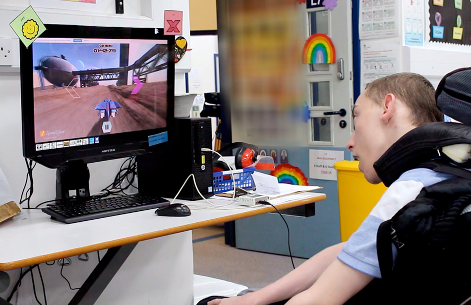 Student in wheelchair in classroom looks at screen with driving game