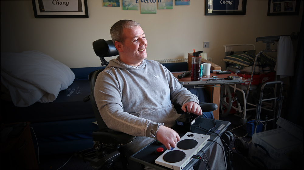 smiling man in wheelchair using an adapted gaming control setup