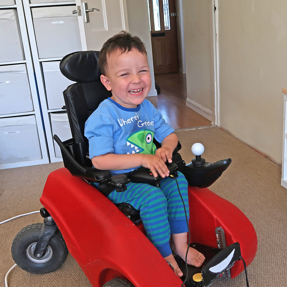 Young child in buggy with hands on adapted controller