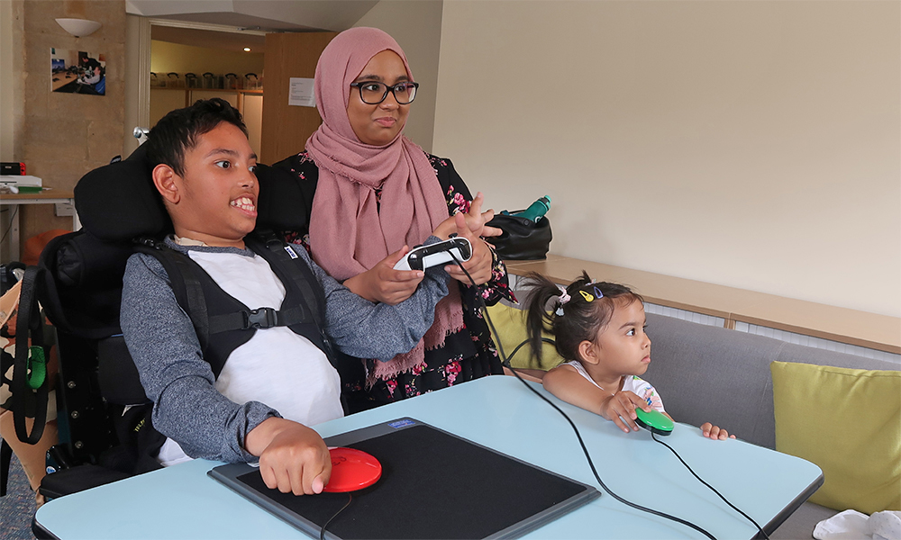 Boy in wheelchair, woman and small child at a table, holding switches 