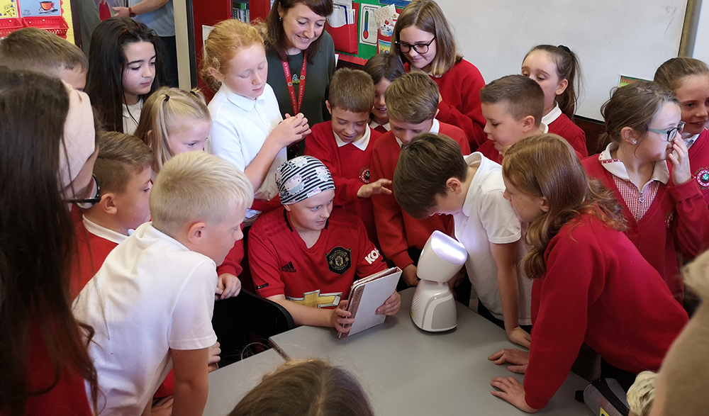 Girl with robot in classroom surrounded by classmates