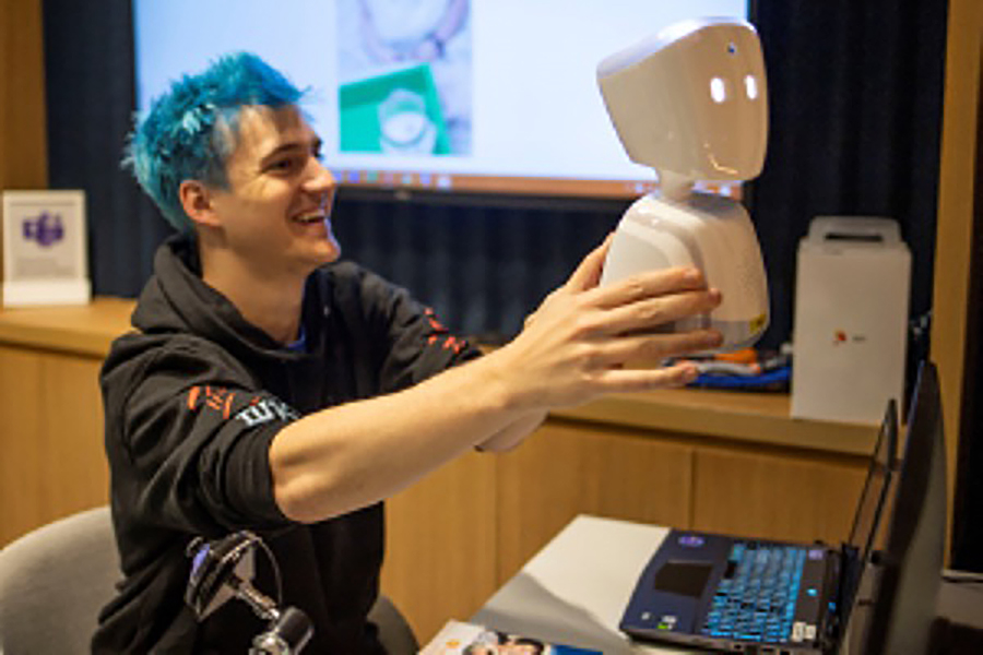 smiling man holding up a small football-sized robot