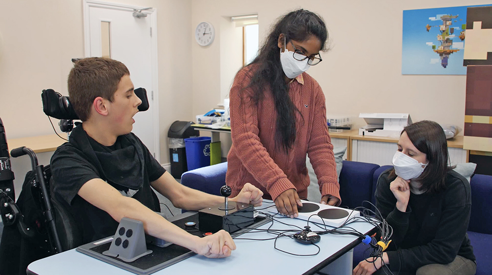 Two women adjust the gaming setup of young man, who looks on