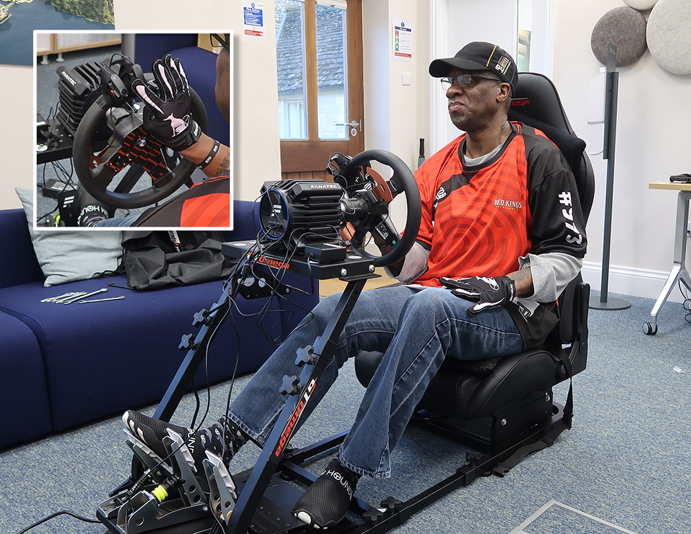 Man in cap sitting in racing sim cockpit, one hand holding the steering wheel 