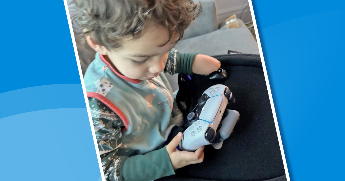 Small boy with curly hair looks down on an adapted gaming controller he's holding