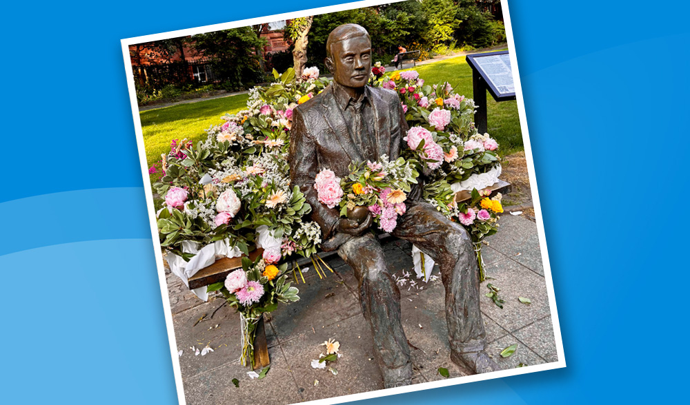 Flowers cover a statue of a man sitting on a bench